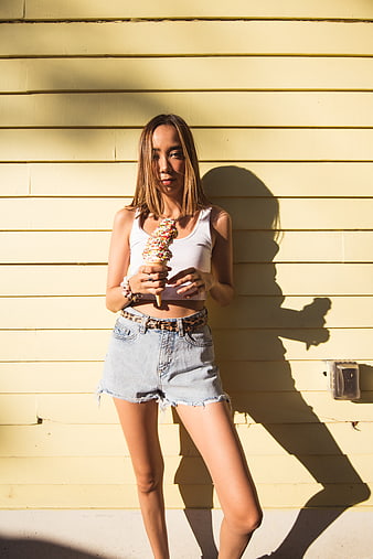 Stylish woman eating ice cream cone against yellow wall