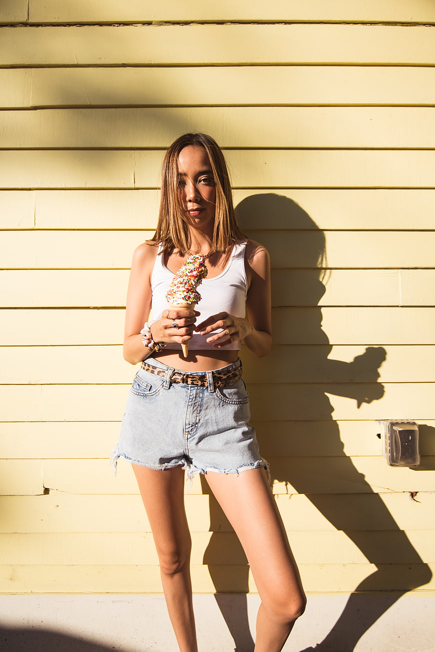 Stylish woman eating ice cream cone against yellow wall