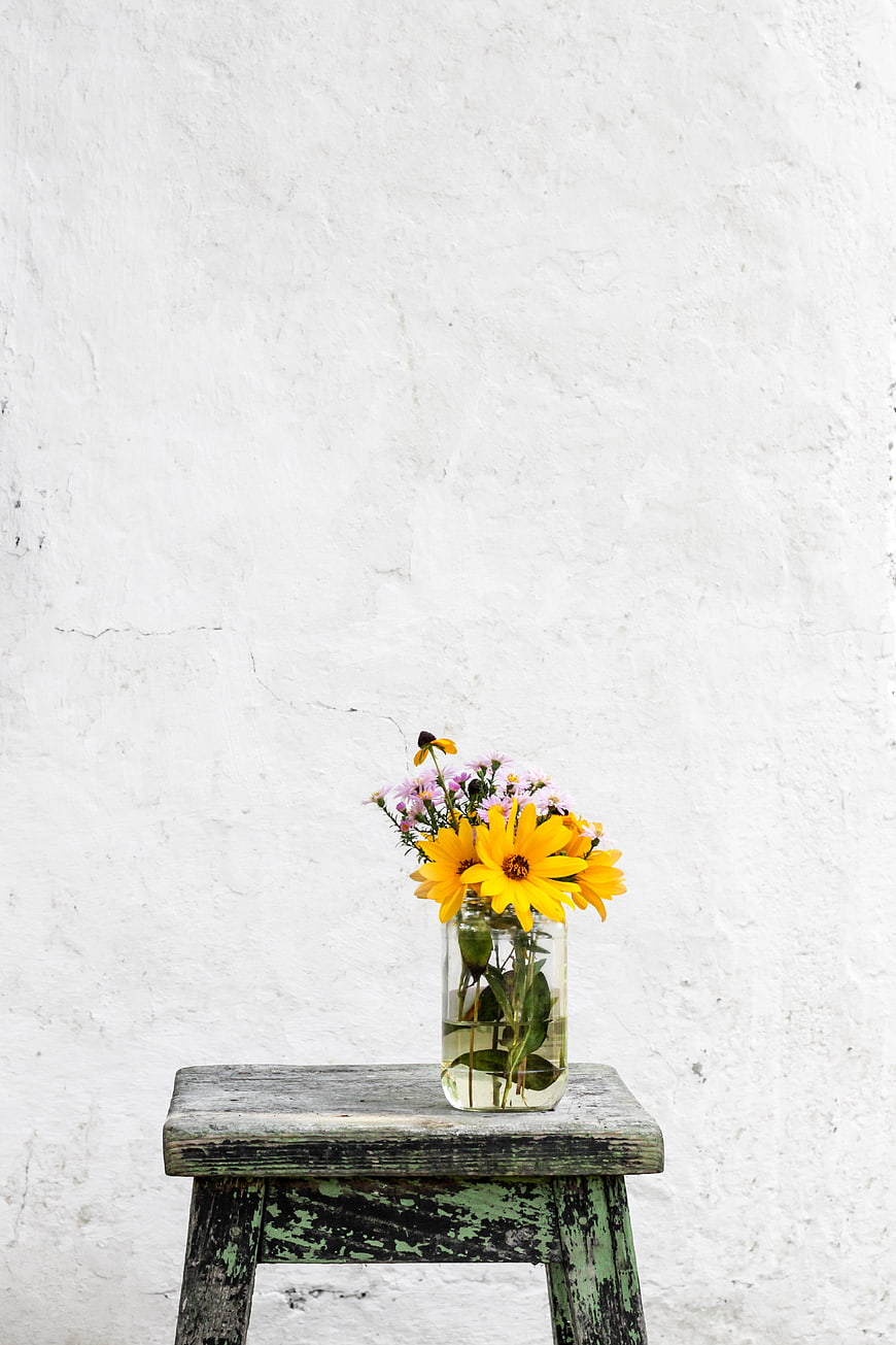 Yellow flowers in glass jar on rustic wooden stool