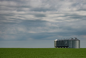 Metal grain silos in green field under cloudy sky