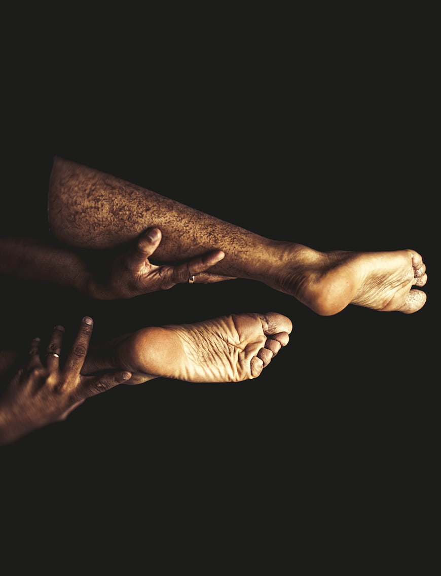 Close-up of hands massaging feet on dark background