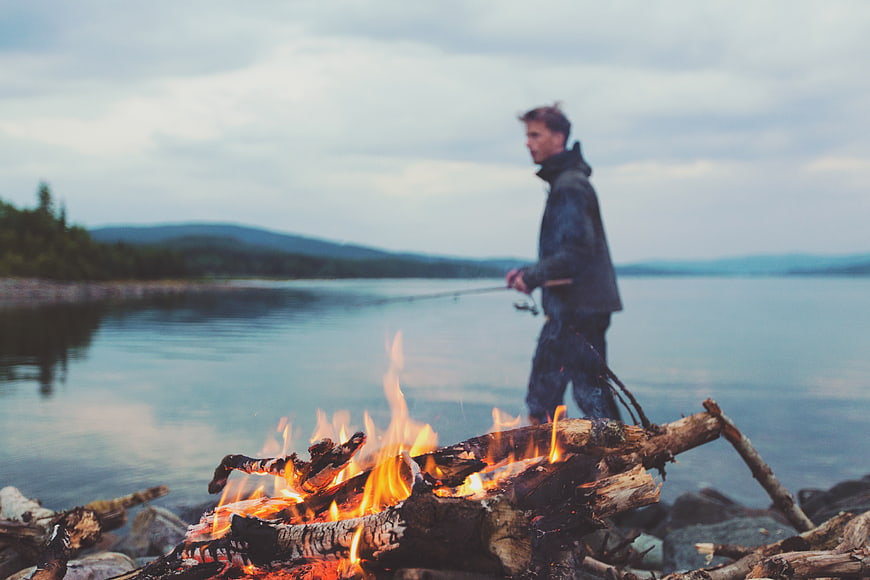Man Fishing by Campfire on Lake Shore