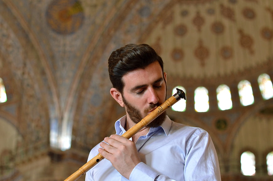 Man playing ney flute in ornate mosque interior