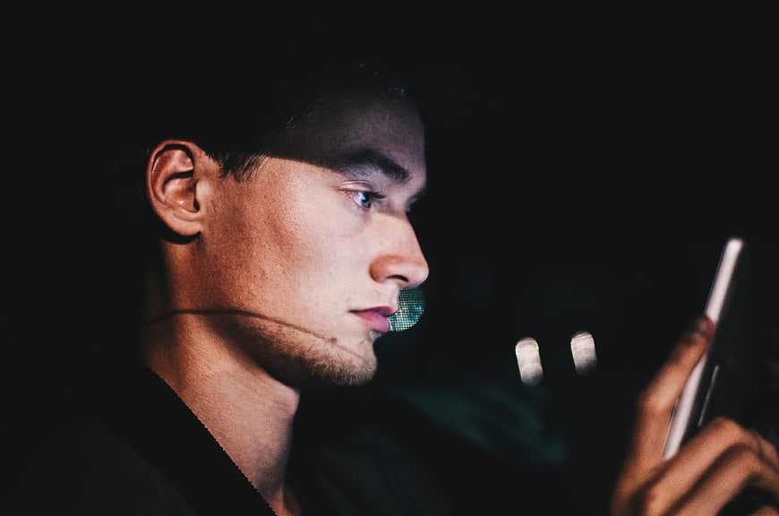Man looking at smartphone screen in dark night setting