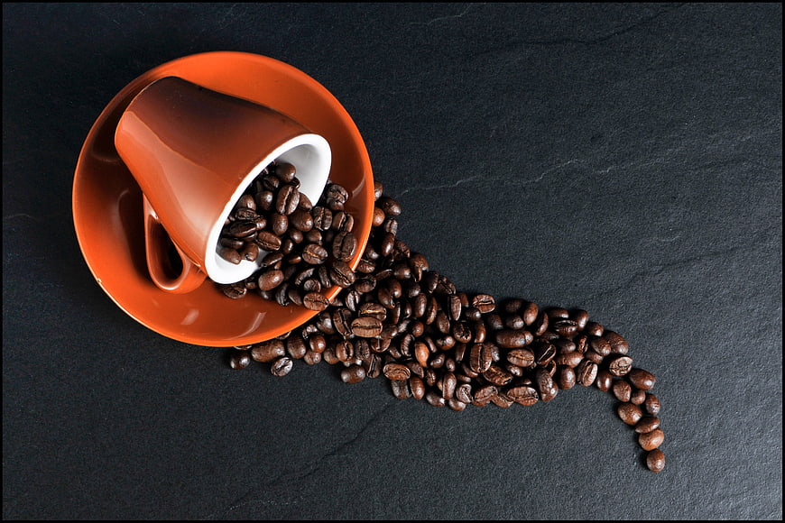 Orange Coffee Cup Spilling Beans on Dark Slate Background