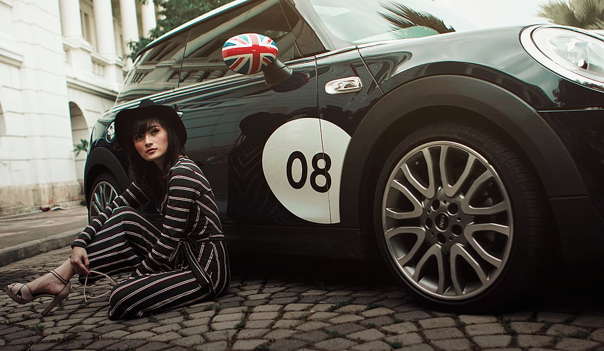 Fashionable Woman Sitting by Black Mini Cooper on Cobblestone Street