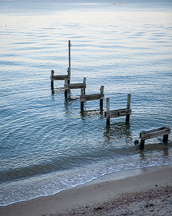 Weathered wooden pier remnants on a calm sandy beach