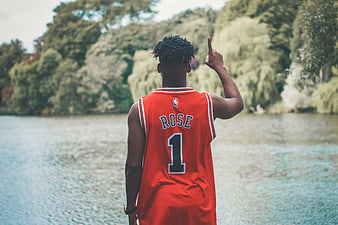 Man in Red Rose Basketball Jersey Pointing Up by Lake