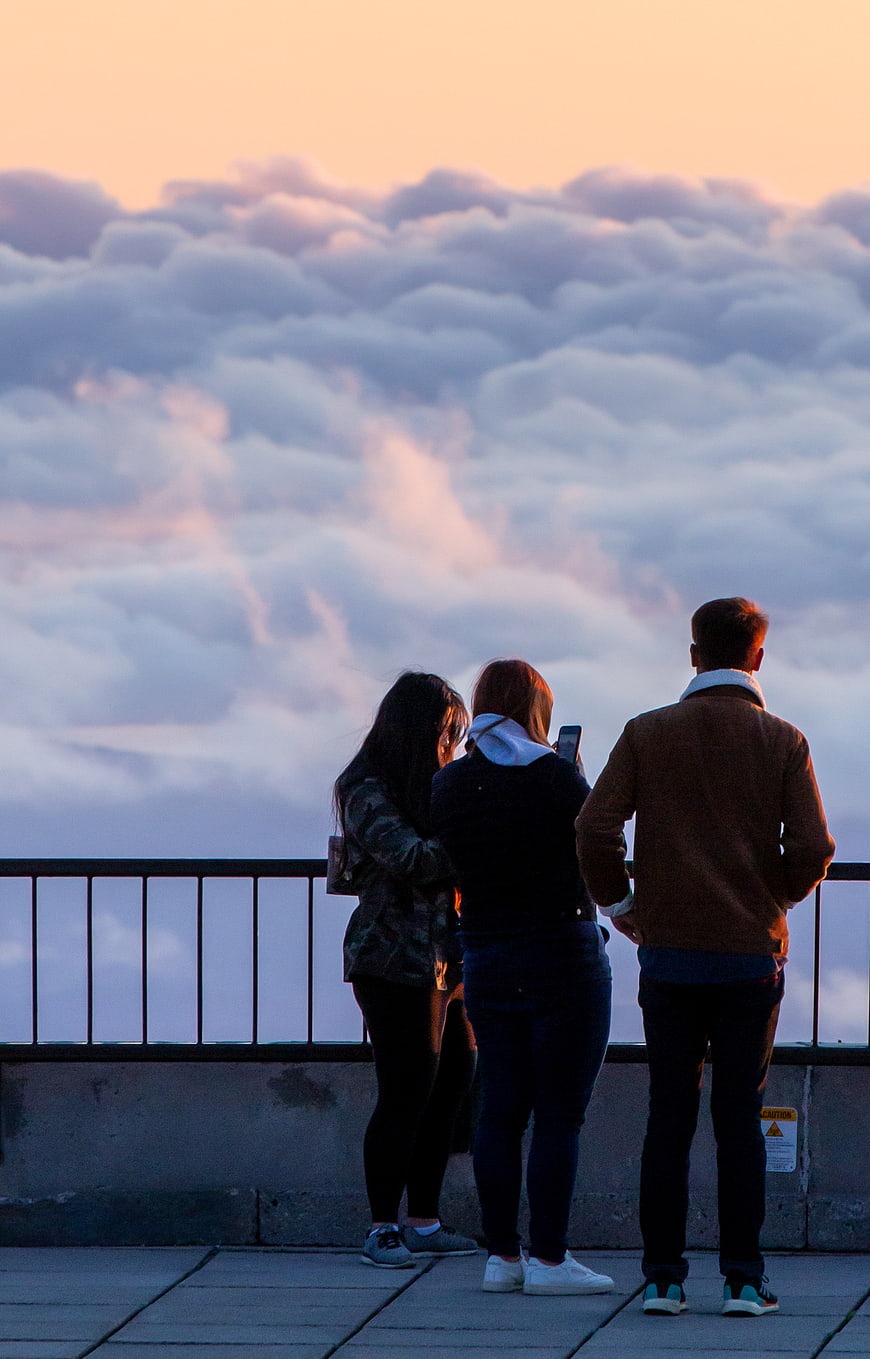 Three people watching sunset over sea of clouds from viewpoint