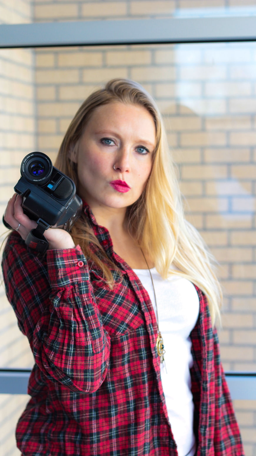 Young female videographer holding camera with brick background