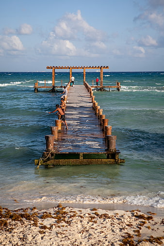 Wooden pier extending into turquoise ocean with people fishing