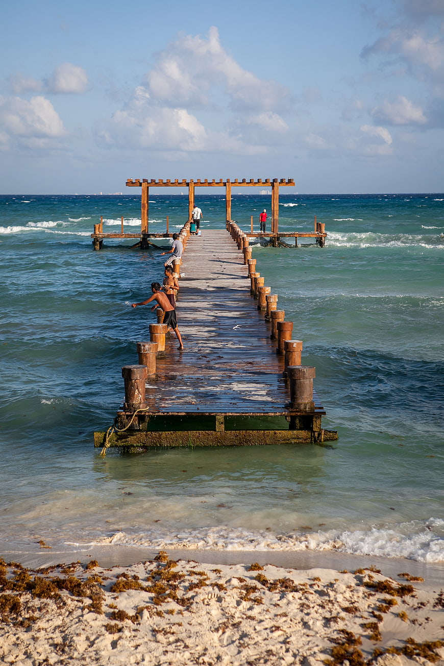 Wooden pier extending into turquoise ocean with people fishing
