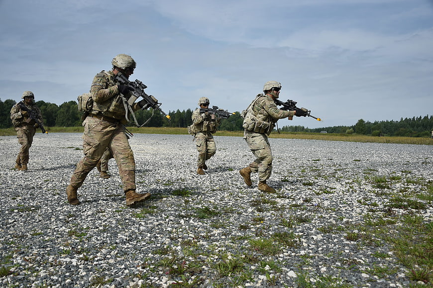 Soldiers in camouflage running with rifles during military training exercise