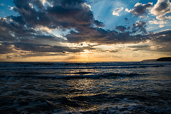Dramatic sunset over ocean with golden sun rays through clouds