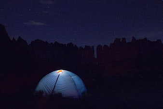 Illuminated camping tent under starry night sky with rock formations