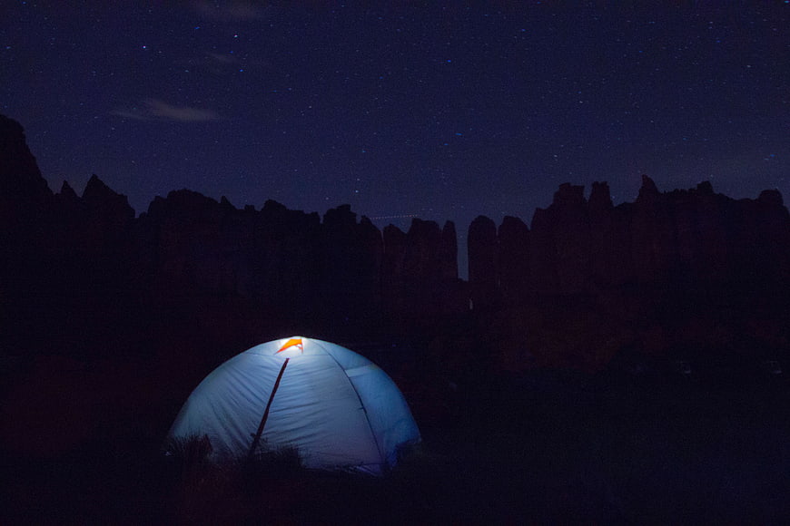 Illuminated camping tent under starry night sky with rock formations
