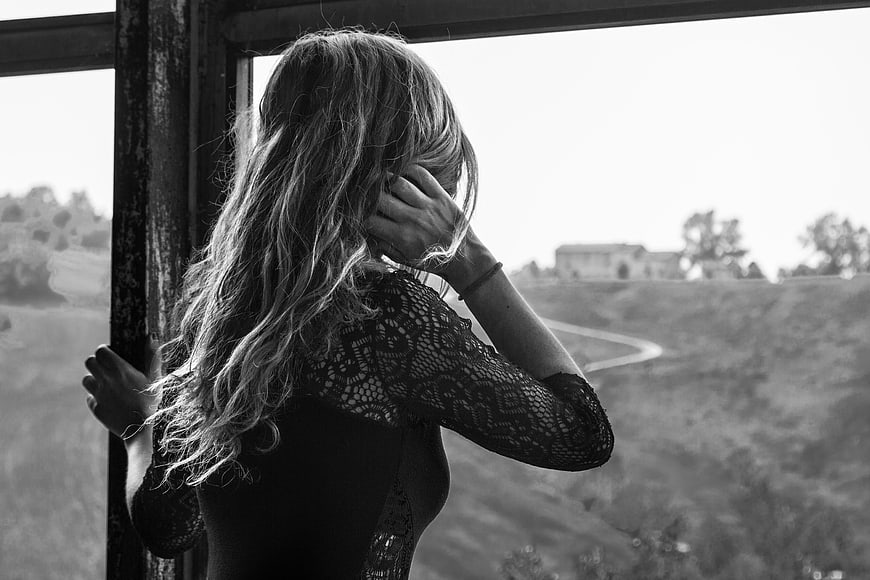 Black and white portrait of a woman looking out a window at a landscape
