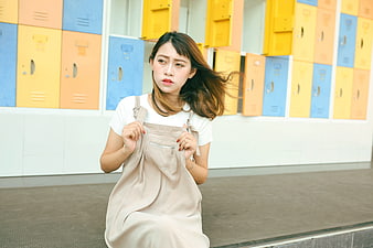 Young Woman in Overalls Sitting in Front of Colorful Lockers