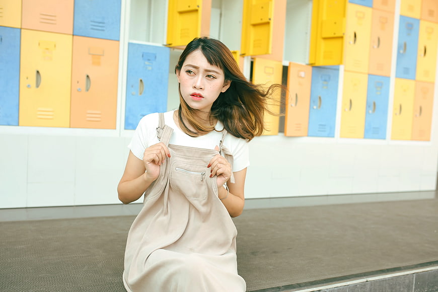 Young Woman in Overalls Sitting in Front of Colorful Lockers