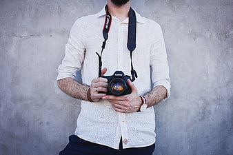 Male Photographer Holding DSLR Camera Against Concrete Wall
