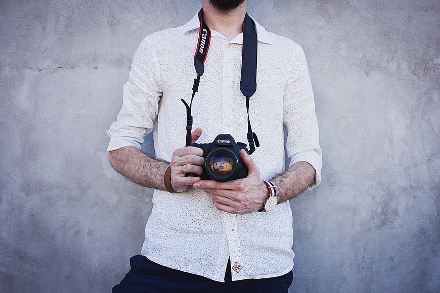 Male Photographer Holding DSLR Camera Against Concrete Wall
