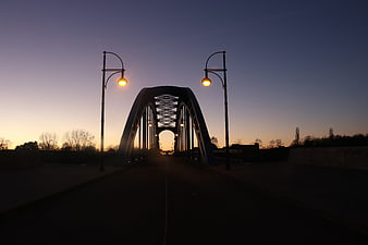 Silhouette of arched bridge at dusk with glowing street lamps