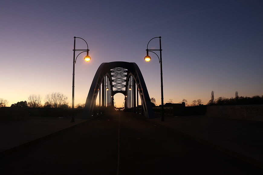 Silhouette of arched bridge at dusk with glowing street lamps