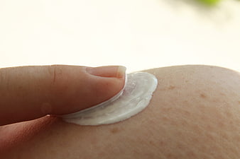 Close-up of finger applying white sunscreen cream to skin