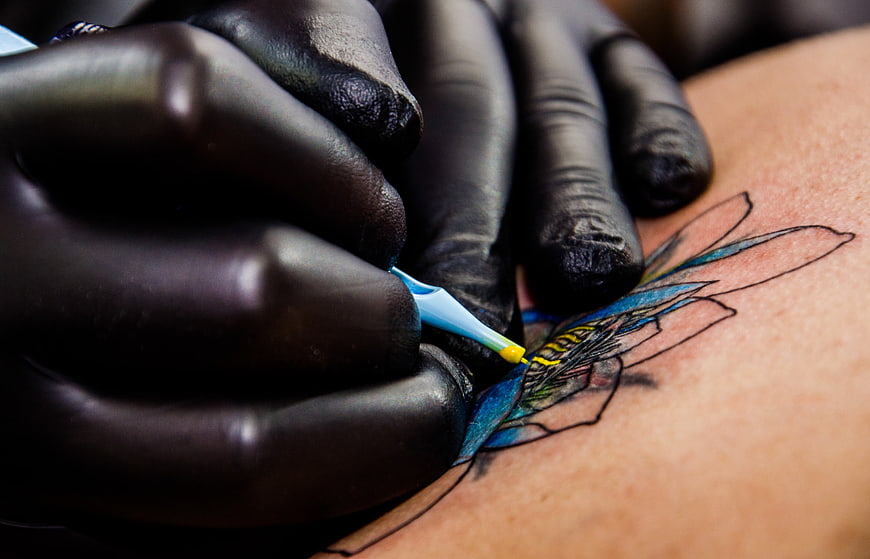 Close-up of tattoo artist applying blue ink to lotus flower design