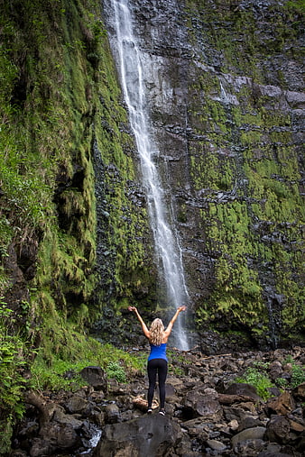Woman with arms raised facing mossy waterfall in nature