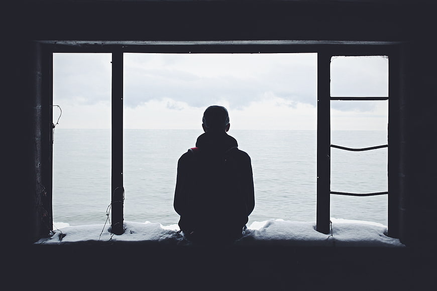 Silhouette of Man Looking Out Window at Ocean in Winter