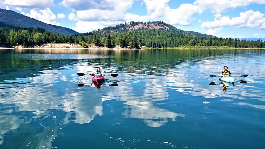 Two people kayaking on a calm lake with mountain reflections
