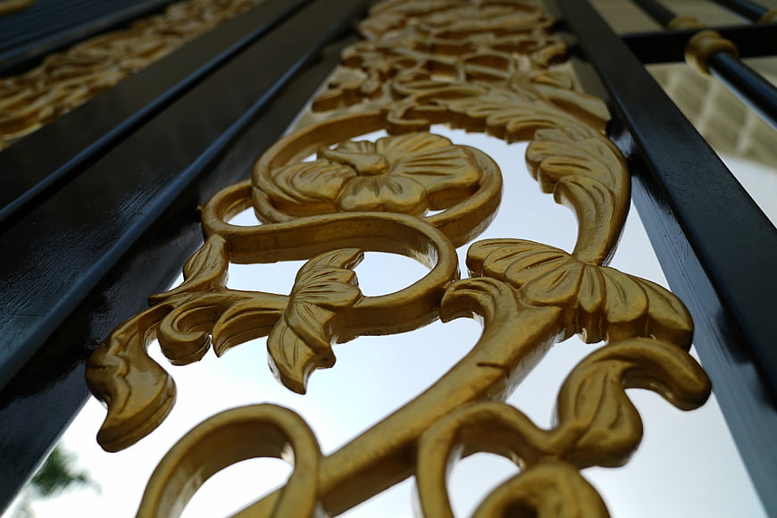 Close-up of ornate golden metalwork on black iron gate