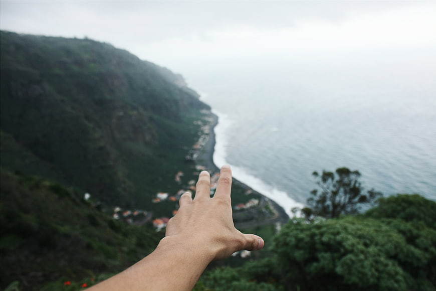 Hand Reaching Out Over Coastal Mountain Landscape