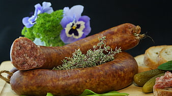 Smoked sausages with herbs, pickles, and bread on wooden board