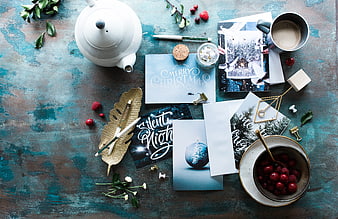 Flat lay of Christmas greeting cards, teapot, and berries on blue background