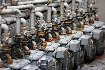 Row of rusty gas meters and pipes against a brick wall
