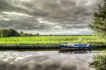 Blue Narrowboat Docked on Canal Under Dramatic Clouds