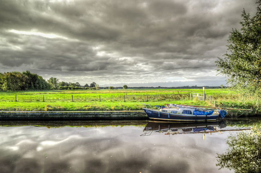 Blue Narrowboat Docked on Canal Under Dramatic Clouds