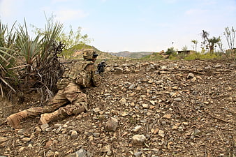 US Army Soldier In Combat Gear Crouching In Rocky Terrain