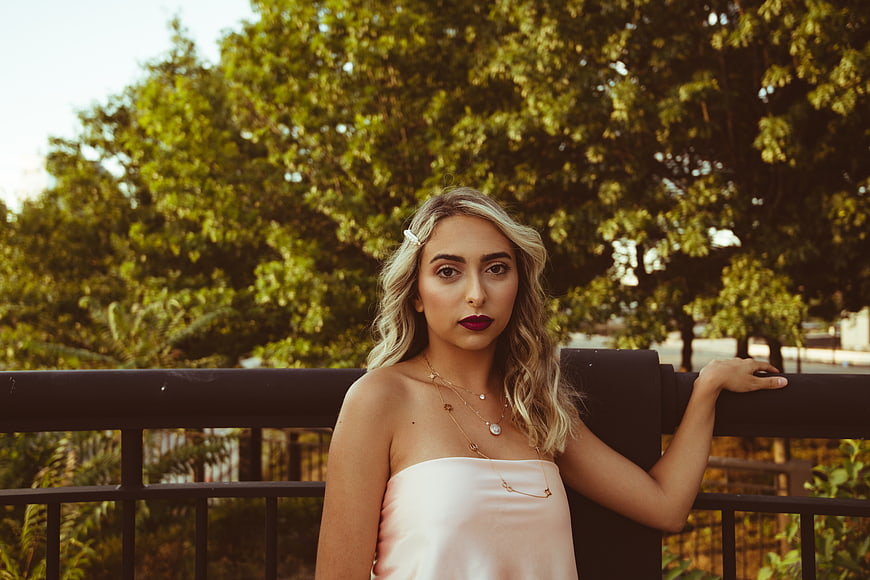 Blonde woman in pink top leaning on railing outdoors