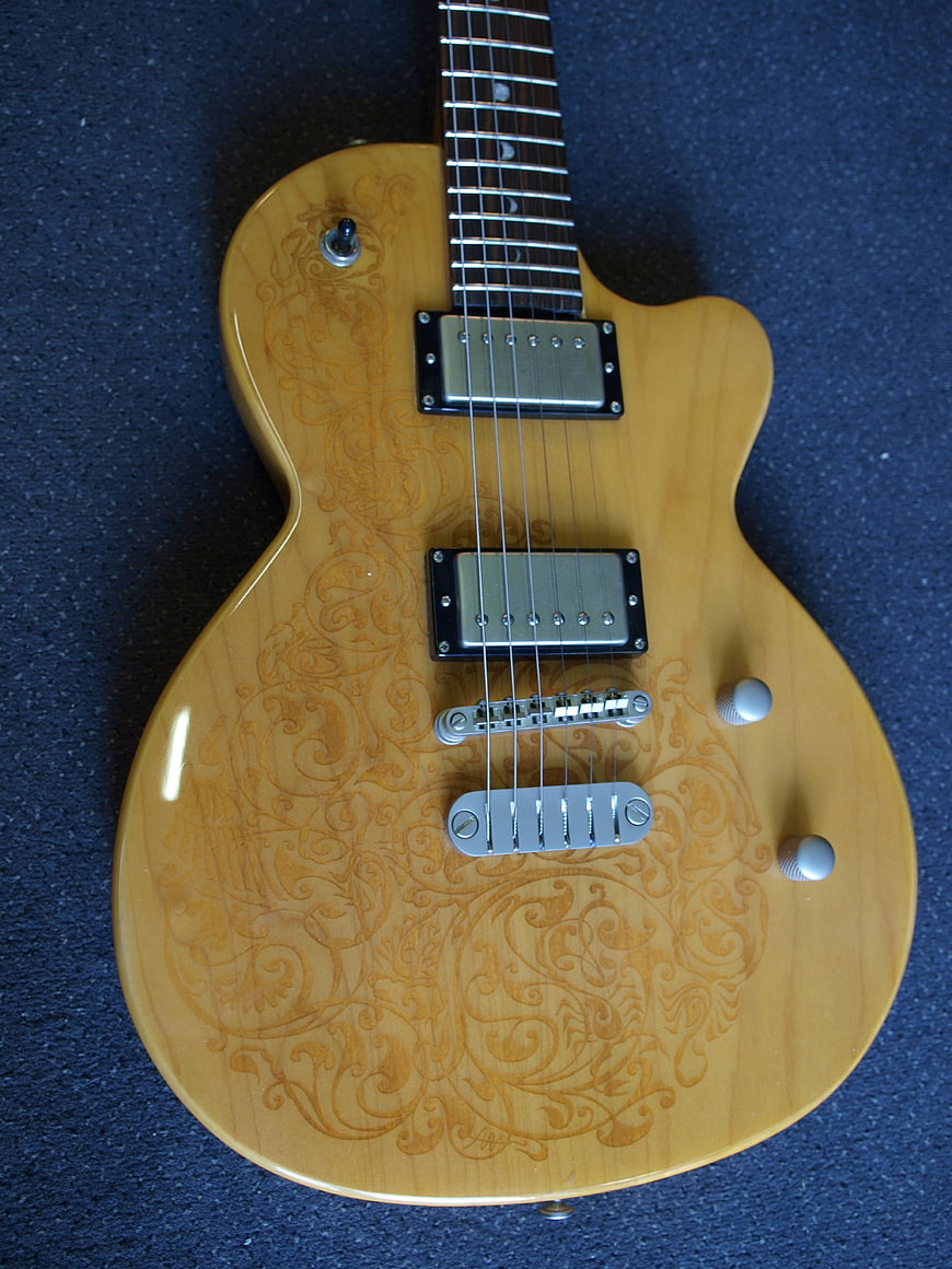 Top-down view of a natural wood electric guitar with intricate carved patterns