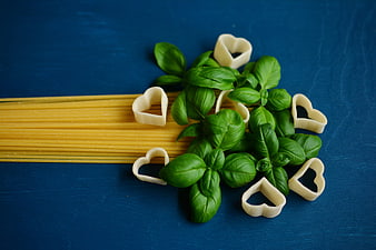 Fresh heart-shaped pasta and basil leaves on blue background