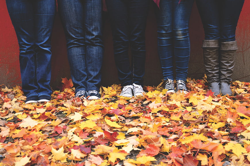 Group of friends standing in autumn leaves wearing jeans