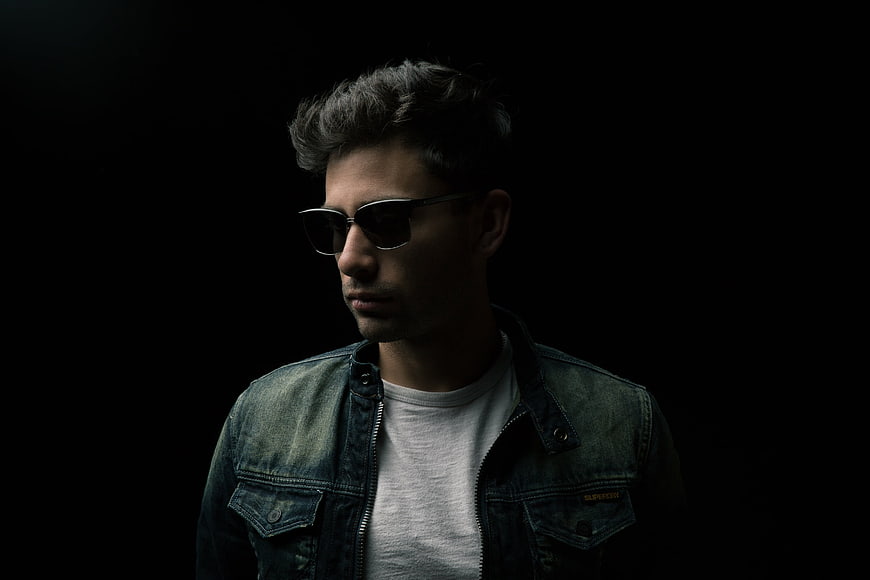Stylish man in sunglasses and denim jacket against black background