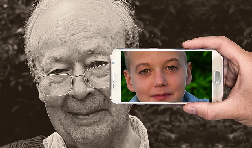 Senior man portrait with smartphone displaying young boy face
