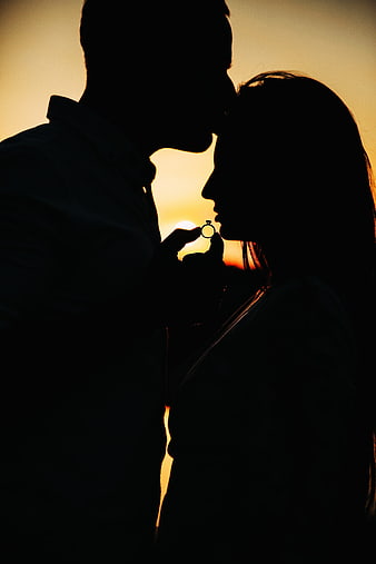 Silhouette of couple with engagement ring at sunset