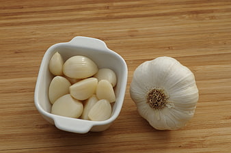 Peeled Garlic Cloves in White Bowl Next to Whole Garlic Bulb on Wooden Surface