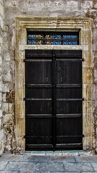 Old black wooden church door with stone frame and iron grille