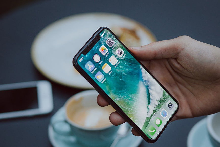 Hand holding smartphone with coffee and pastry background